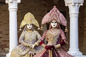 Two women wearing Indian style costumes and masks pose in the cloisters of Chiesa di San