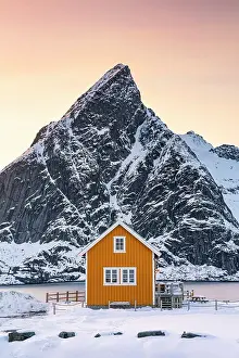 Yellow Rorbu with majestic Olstind peak covered with snow on background, Sakrisoy, Reine, Nordland, Lofoten Islands, Norway
