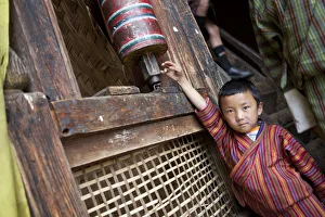 Prayer Gallery: A young boy playing with a prayer wheel in the Thangbi Mani monastery in Bhutan