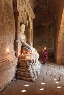Young Buddhist monk prays in front of a statue of Buddha in a temple in Bagan, Myanmar