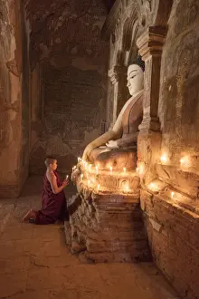 Young Buddhist monk prays in front of a statue of Buddha in a temple in Bagan, Myanmar