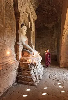 Candles Prints: Young Buddhist monk prays in front of a statue of Buddha in a temple in Bagan, Myanmar