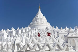 Two young Buddhist monks run and jump across the white walls of Hsinbyume Pagoda, Mingun