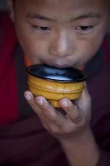 A young monk drinking milk from a wooden bowl in Bhutan