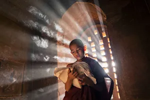 A young monk reading by a window inside a temple, UNESCO, Bagan, Mandalay Region, Myanmar