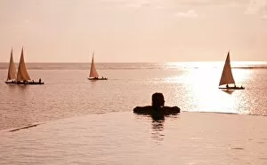 Sun Rise Gallery: Zanzibar, Matemwe Bungalows. A tourist stands at the edge of an infinity pool watching the Dhows